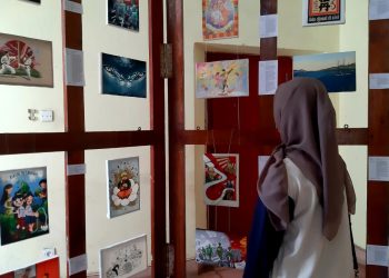 Seorang wanita sedang mengamati lukisan pada pameran Okasan: Matahari, Laut, dan Propaganda, Minggu (26/05).Foto: Dokumentasi Pribadi.