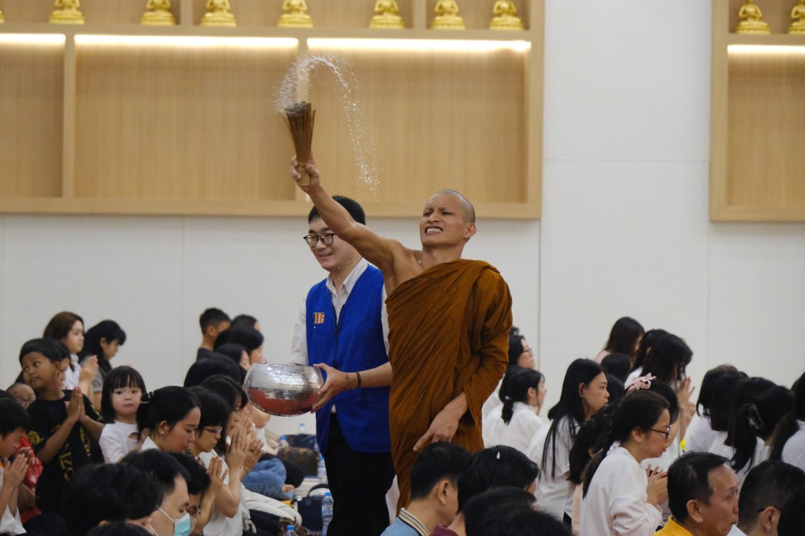 Seorang bhikku menyiramkan air suci kepada para umat