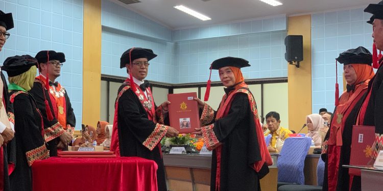 Prof Dr Gustiana A Kambo SIP MSi (kanan) saat menerima buku kode etik anggota Dewan Profesor Unhas pada pengukuhan dan penerimaan anggota Dewan Profesor Unhas di Ruang Rapat Senat Lantai 2, Gedung Rektorat Unhas, Selasa (05/08). Foto: IDENTITAS/Masyita