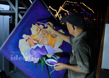 Pria paruh baya sedang melukis gambar bunga dengan gaya realis.